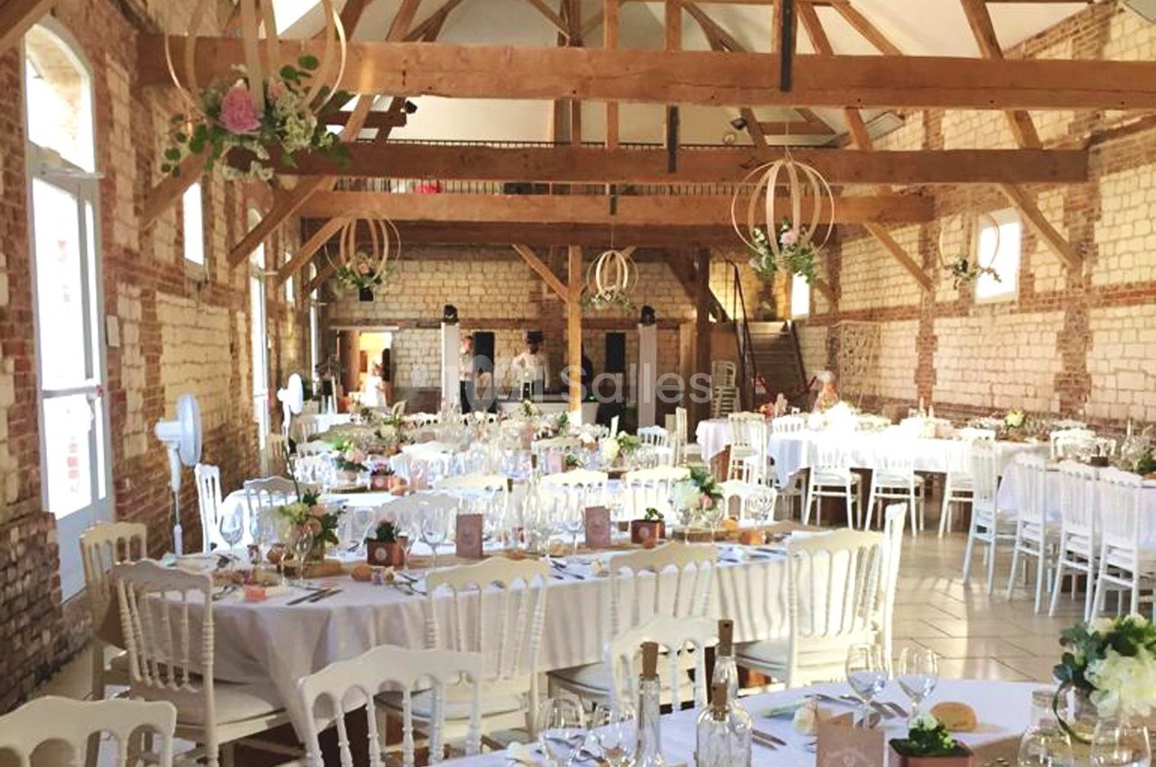 Salle de réception lumineuse avec poutres apparentes, tables décorées pour un événement festif.