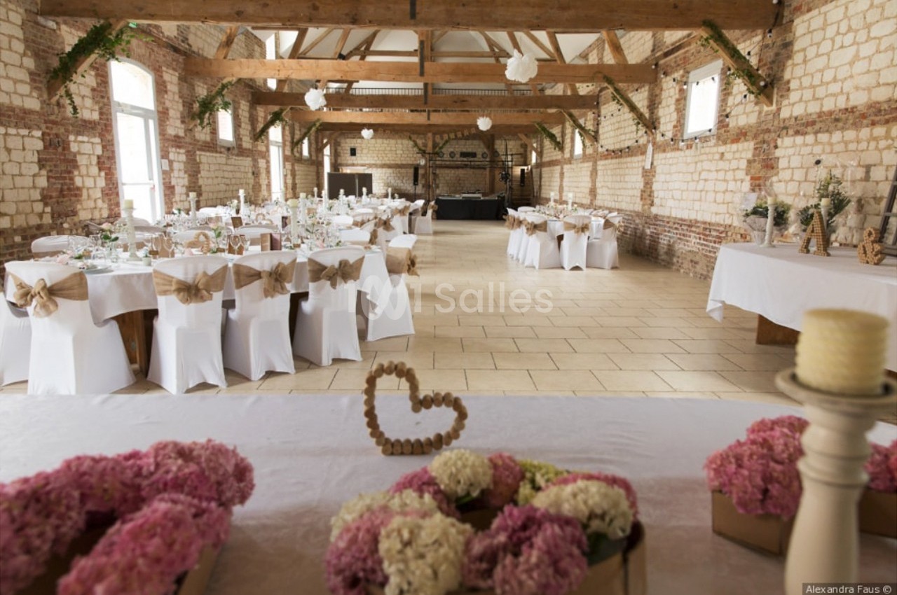Salle de réception décorée pour un mariage, avec tables dressées, chaises ornées de nœuds et fleurs en centre de table.