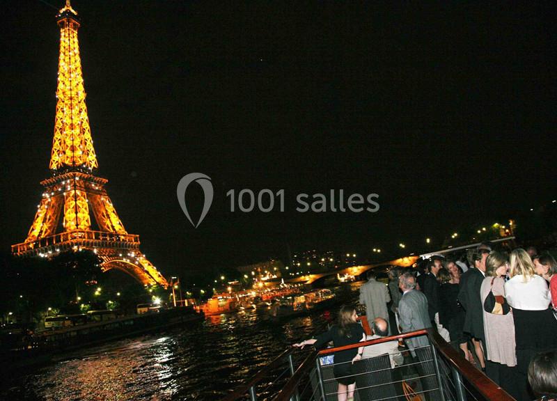 Des personnes sur un bateau naviguent la nuit près de la Tour Eiffel illuminée.