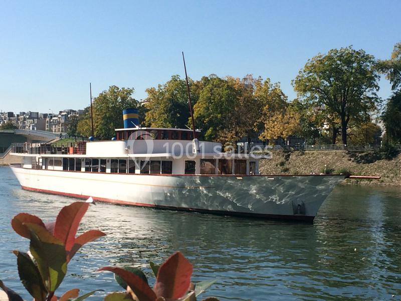 Bateau blanc naviguant sur une rivière bordée d'arbres sous un ciel dégagé.