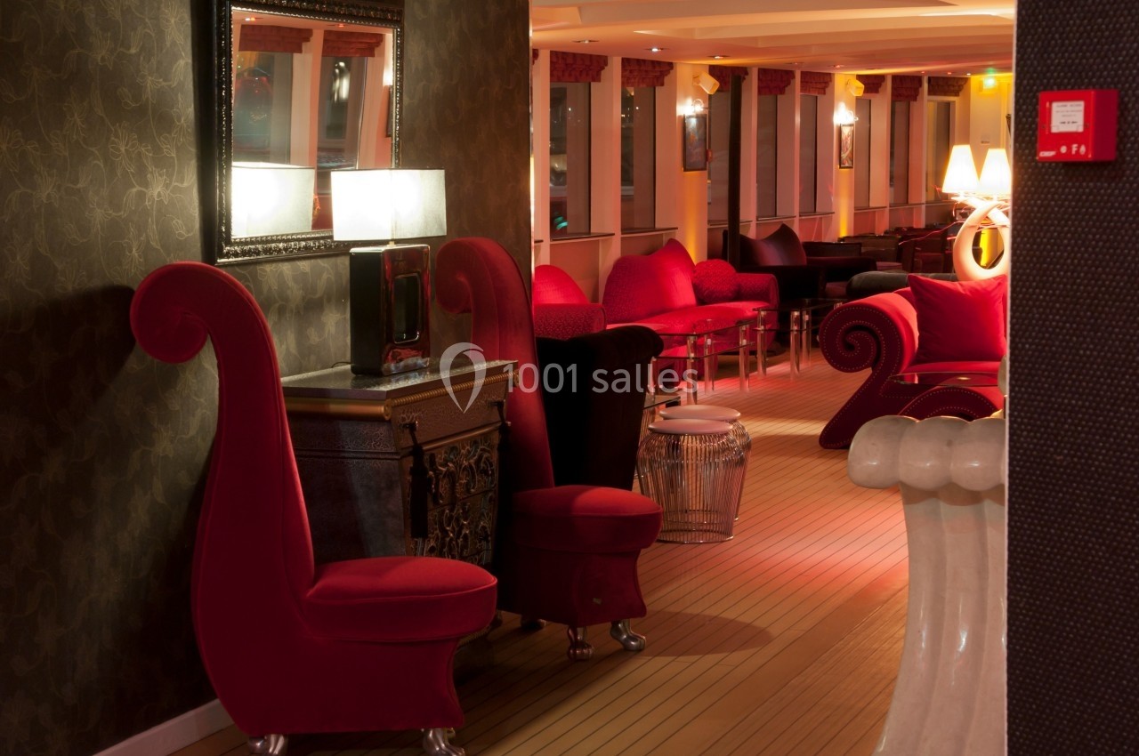 Salon élégant avec fauteuils rouges, éclairage tamisé, miroir mural et mobilier décoratif sur un sol en bois clair.