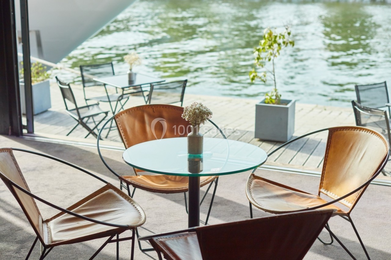 L'Atelier du France Table ronde en verre entourée de fauteuils en cuir, placée près d'une terrasse donnant sur un plan d'eau.