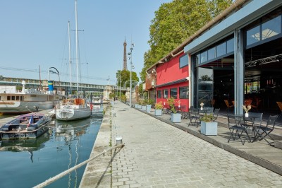 Miniature L'Atelier du France Bateau amarré le long d'un quai, avec une table dressée et des verres à vin sur le pont arrière.