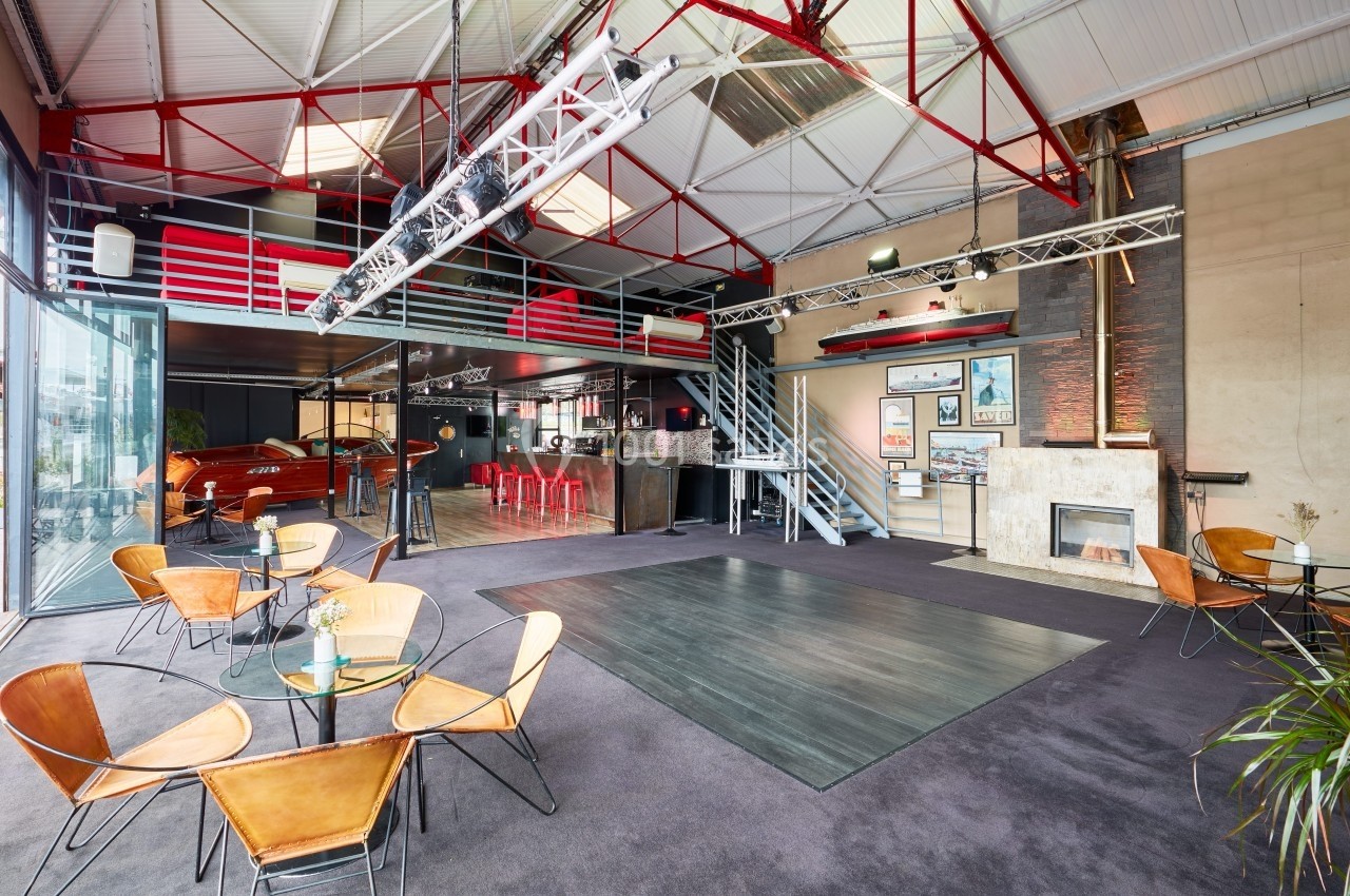 L'Atelier du France Salle spacieuse avec mezzanine, tables en verre, chaises design, bar rouge et grande baie vitrée laissant entrer la lumière.