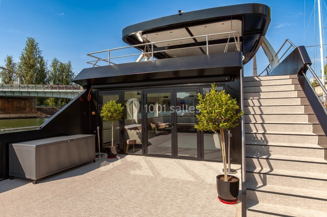 La Perle Noire Terrasse d'un bateau moderne avec escalier, plantes en pot et grandes baies vitrées donnant sur un intérieur lumineux.