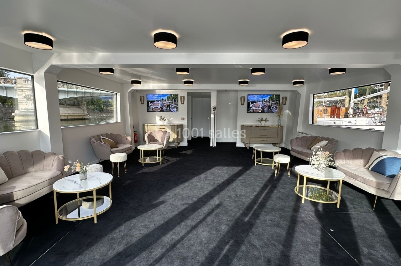 La Perle Noire Salle lumineuse avec canapés, tables basses et décorations florales, offrant une vue sur l'extérieur par de grandes fenêtres.