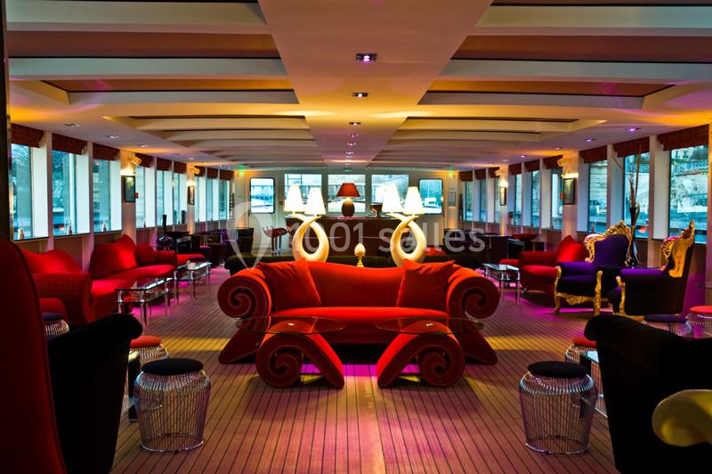 Le Clipper Paris Salon élégant avec canapés rouges, éclairage tamisé et grandes fenêtres offrant une vue extérieure.