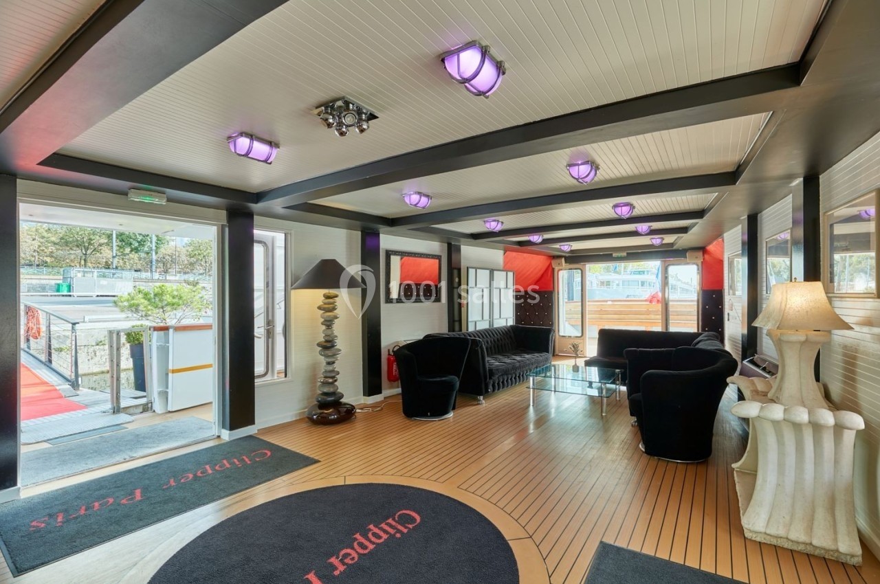 Le Clipper Paris Intérieur lumineux d'un salon avec canapés noirs, lampes design et vue sur l'extérieur par des baies vitrées.