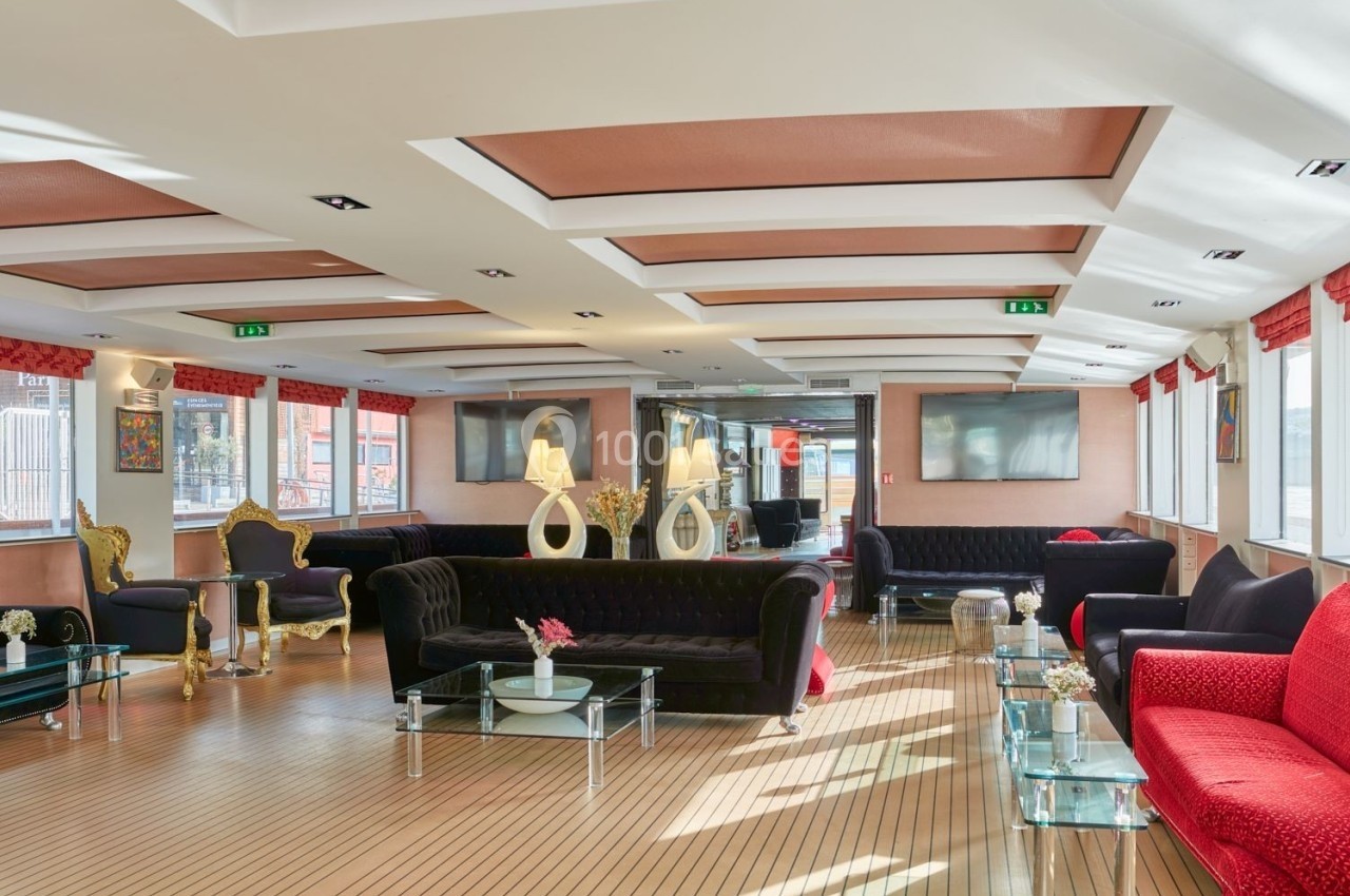 Le Clipper Paris Salon spacieux avec canapés noirs et rouges, tables basses en verre, éclairage naturel et décoration élégante.