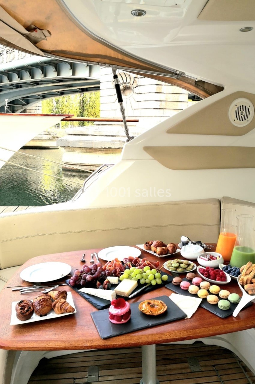 Le James Petit-déjeuner composé de viennoiseries, fruits, macarons et jus, servi sur une table en bois à bord d'un bateau.