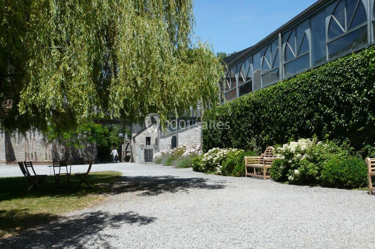 Allée gravillonnée bordée de bancs, de fleurs et de verdure, avec un bâtiment vitré en arrière-plan.