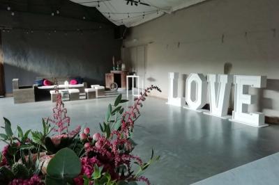 Salle de réception décorée avec des tables rondes dressées, des chaises blanches et un plafond orné de guirlandes suspendues.