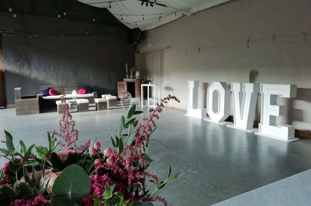 Salle décorée pour un événement avec des fleurs au premier plan et des lettres lumineuses formant ’LOVE’ en arrière-plan.