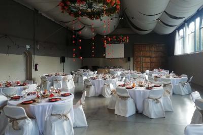 Salle de réception décorée avec des tables rondes dressées, des chaises blanches et un plafond orné de guirlandes suspendues.