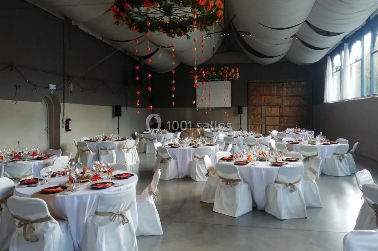Salle de réception décorée avec des tables rondes dressées, nappes blanches et guirlandes suspendues au plafond.