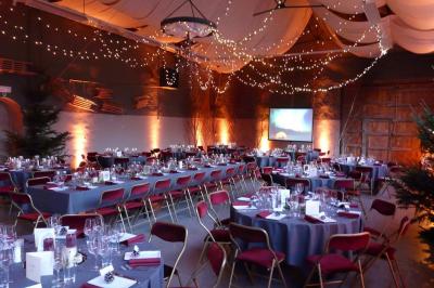 Salle de réception décorée avec des tables rondes dressées, des chaises blanches et un plafond orné de guirlandes suspendues.