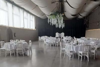Salle de réception décorée avec des tables rondes dressées, des chaises blanches et un plafond orné de guirlandes suspendues.