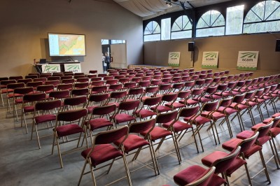 Salle décorée pour un repas festif avec longues tables dressées, guirlandes lumineuses et grand sapin illuminé.