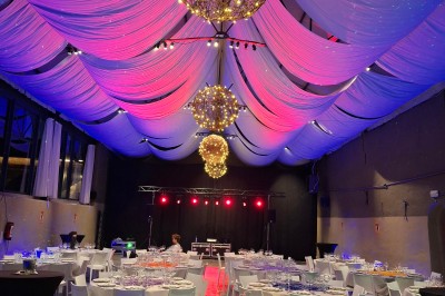 Salle décorée pour un repas festif avec longues tables dressées, guirlandes lumineuses et grand sapin illuminé.