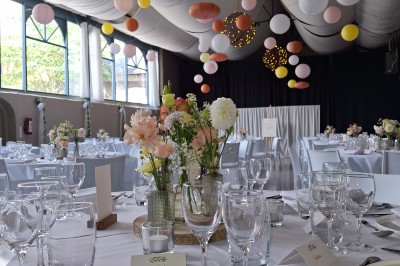 Salle décorée pour un repas festif avec longues tables dressées, guirlandes lumineuses et grand sapin illuminé.