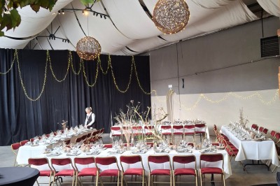 Salle décorée pour un repas festif avec longues tables dressées, guirlandes lumineuses et grand sapin illuminé.