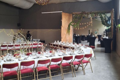 Salle décorée pour un repas festif avec longues tables dressées, guirlandes lumineuses et grand sapin illuminé.