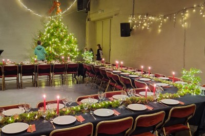 Salle décorée pour un repas festif avec longues tables dressées, guirlandes lumineuses et grand sapin illuminé.