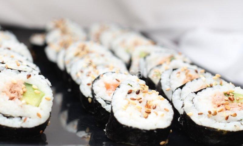 Assortiment de makis au saumon et avocat, garnis de graines de sésame, disposés sur un plateau noir.