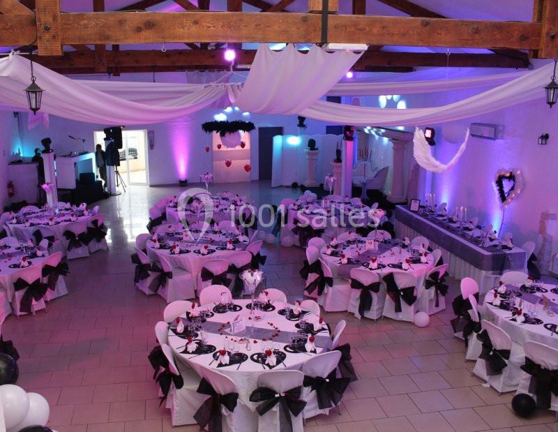 Salle de réception décorée avec des tables rondes dressées, nappes blanches et nœuds noirs, éclairage tamisé.