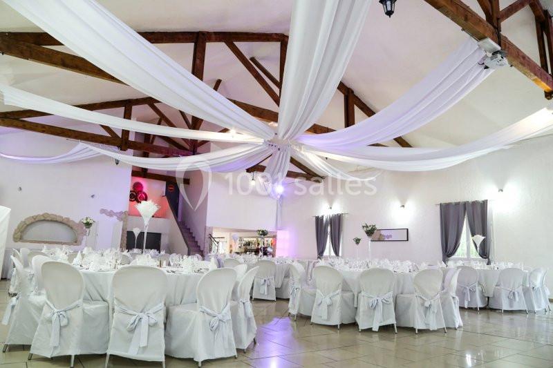 Salle de réception lumineuse avec plafond en poutres apparentes décoré de drapés blancs et tables dressées.