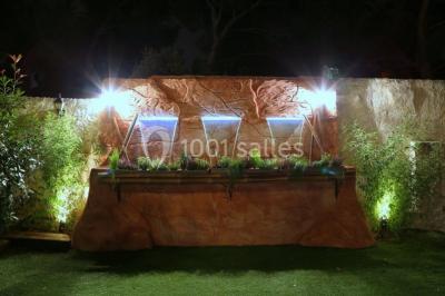 Mur en pierre ocre avec jardinières en bois garnies de fleurs colorées, entouré de végétation et éclairé par la lumière du…