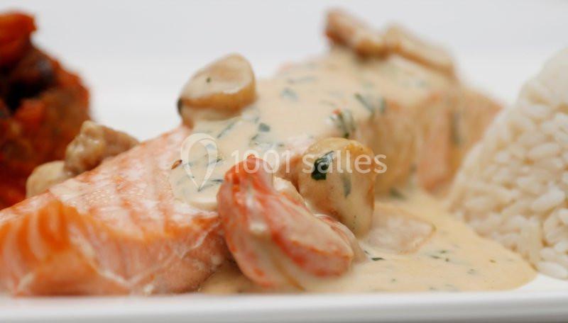 Filet de saumon nappé de sauce crémeuse aux champignons, accompagné de riz blanc et d'un accompagnement en arrière-plan.