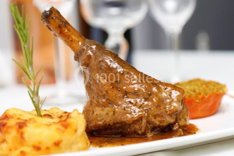 Jarret d'agneau braisé avec sauce, accompagné d'un gratin de pommes de terre et d'une tomate farcie, servi sur assiette…