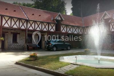 Bâtisse en pierre avec toit en tuiles, entourée de verdure, chemin en gravier et un chien sur la pelouse.