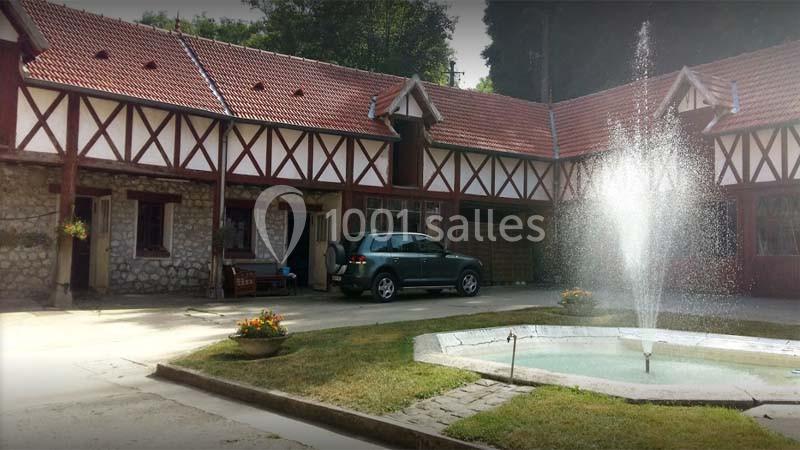 Cour intérieure avec une fontaine centrale, entourée de bâtiments à colombages et toit en tuiles rouges.