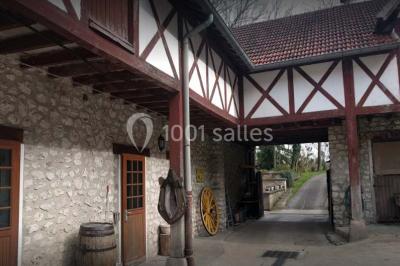 Bâtisse en pierre avec toit en tuiles, entourée de verdure, chemin en gravier et un chien sur la pelouse.