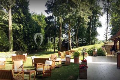 Bâtisse en pierre avec toit en tuiles, entourée de verdure, chemin en gravier et un chien sur la pelouse.