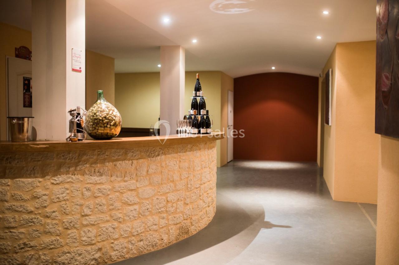 Comptoir en pierre avec bouteilles de vin et verres, dans un couloir éclairé aux murs beige et rouge.