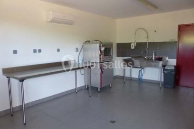 Bâtiment à un étage avec toit en tuiles, entouré de chemins, de pelouse et de vignes en arrière-plan.