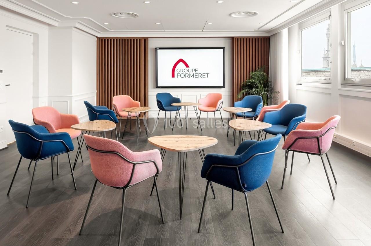 Salle de réunion lumineuse avec des chaises colorées disposées en cercle et un écran affichant un logo.