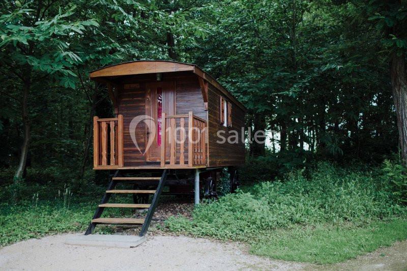 Roulotte en bois avec terrasse, située dans une clairière entourée d'arbres et de végétation dense.