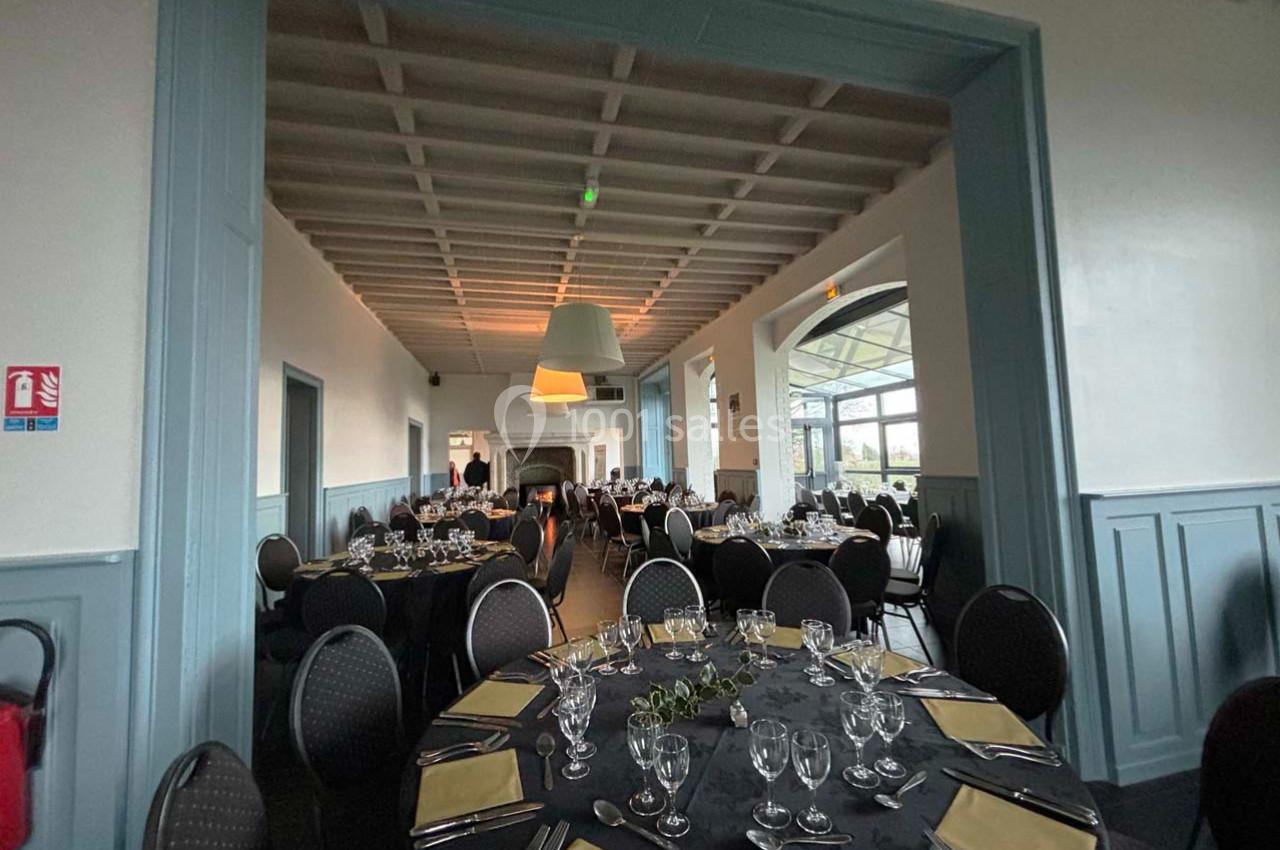 Salle de réception élégante avec tables rondes dressées, nappes noires, serviettes jaunes et chaises noires.