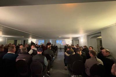 Grande maison à colombages éclairée en vert la nuit, avec des fenêtres illuminées et un porche couvert.