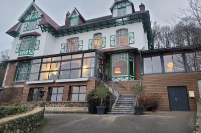 Grande maison à colombages éclairée en vert la nuit, avec des fenêtres illuminées et un porche couvert.
