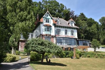 Grande maison à colombages éclairée en vert la nuit, avec des fenêtres illuminées et un porche couvert.