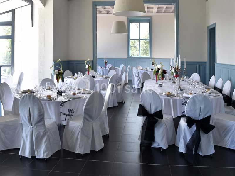 Salle de réception élégamment décorée avec des tables rondes, nappes blanches et chaises ornées de nœuds noirs.