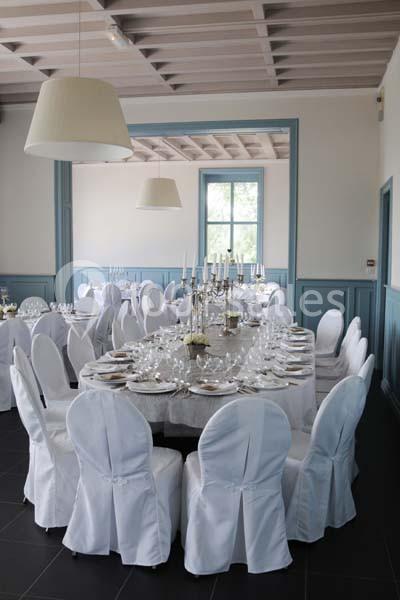 Salle de réception élégante avec tables rondes dressées, nappes blanches et chandeliers, éclairée par des suspensions…