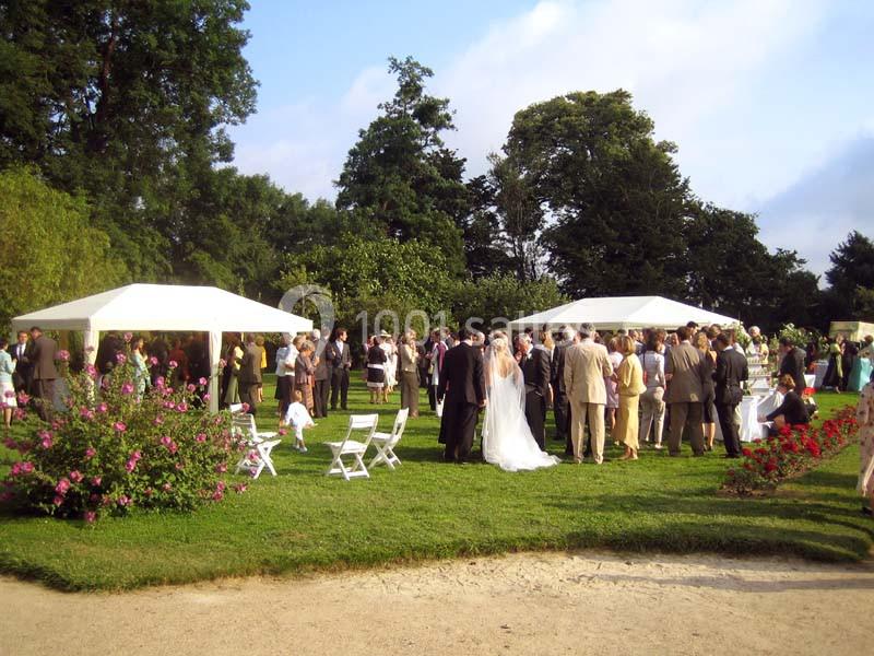 Groupe de personnes rassemblées dans un jardin pour une réception en plein air, avec des tentes blanches et des chaises.