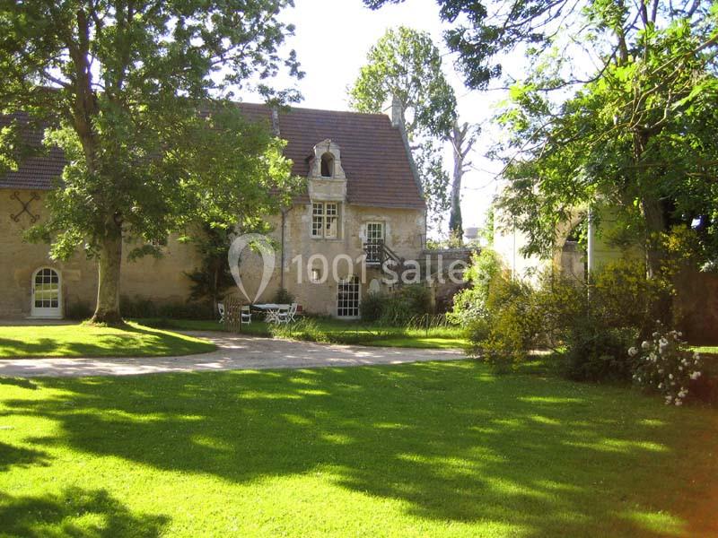 Bâtisse ancienne en pierre entourée d'arbres et d'une pelouse verdoyante sous un ciel dégagé.