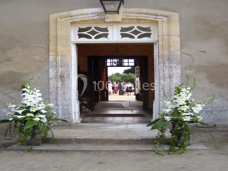 Entrée d'un bâtiment ancien avec porte ouverte, décorée de deux arrangements floraux blancs sur des piédestaux.